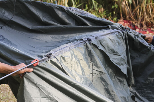 Close up outdoor shot showing hand holding pole to set up black waterproof camping tent flysheet in nature with focused preparation for overnight shelter adventure