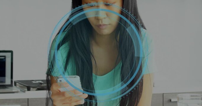 Woman raising phone in kitchen, tapping screen to review cyber security HUD circling head and torso