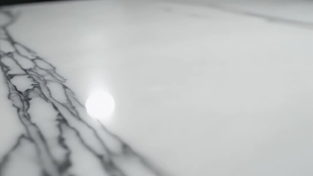 Close-up view of a white marble surface with dark veins and bright light reflection.