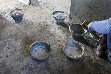 Dedicated laborer busy working with heavy cement buckets on messy concrete floor at rugged construction site representing hard work industrial concept and building progress