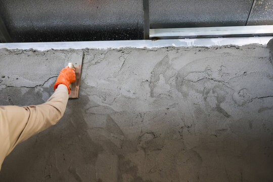 Professional construction worker carefully smoothing wet cement surface using hand trowel creates solid foundation for industrial building project with focused attention to detail