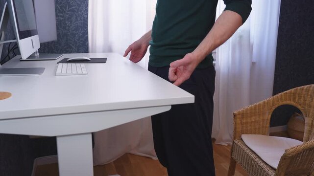 Lowering adjustable desk and sitting down at home office workstation