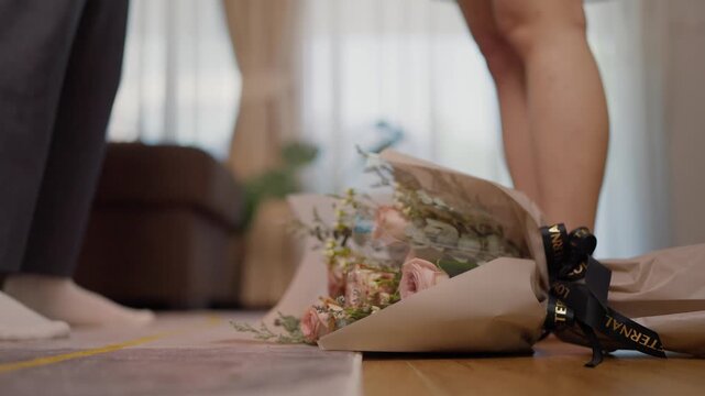 A bouquet of roses falling on the floor in slow motion, with a couple arguing in the background on Valentine�s Day, concept of disappointment and heartbreak in love.