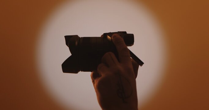 A silhouette of a hand holding a camera against a warm, softly lit backdrop, capturing the essence of photography. Backstage photo shoot.