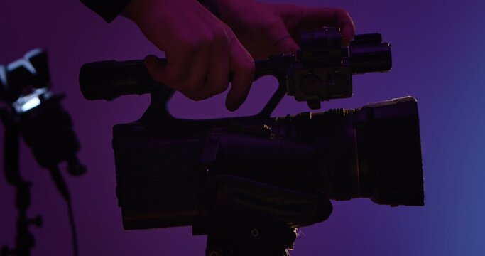 Close up silhouette of hands operating a professional video camera against a purple background. Backstage photo shoot.