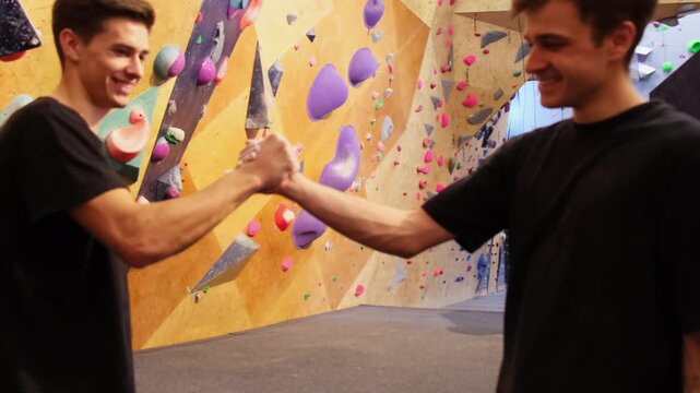 Young people joyfully shake hands before difficult climb on spray wall with hooks. Men hold hands demonstrating team spirit