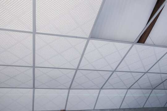 Low angle view of broken white ceiling with damaged panel and suspended grid texture showing neglected condition inside old office building needing repair maintenance construction work