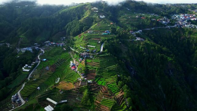 Slow side left aerial over Atok Benguet, Halsema Highway former highest mountain area in the Philippines showing a zigzag highway leading into lush vegetable fields a rural mountain farming.