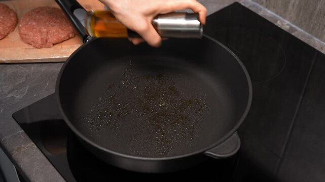 Woman sprays oil on a hot frying pan. Preparing to cook food.
