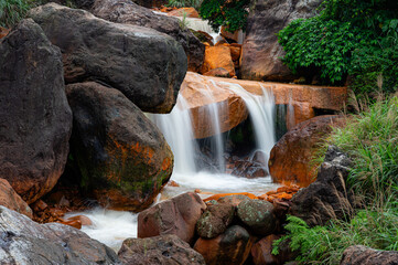 Long exposure view of flowing water near Jiufen, Taiwan, smoothing over rust-colored mineral rocks and dark black stones, creating a calm, abstract composition with rich textures and contrast.

