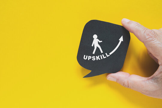 hand hold UPSKILL text , increasing arrow and man walking icon on real black speech bubble paper cut on yellow background
