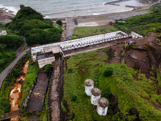 Aerial view of a river winding past the abandoned industrial terraces of the 13 Levels mining site near Jiufen, Taiwan, flowing into the sea, highlighting the interplay of industrial ruins and water
