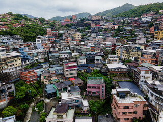Aerial view of the mountain town of Jiufen in Taiwan, with dense hillside houses, winding streets, and dramatic terrain overlooking the coast, creating a layered and atmospheric townscape.

