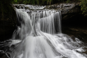 Long-exposure view of a smaller waterfall at Shifen, Taiwan, with silky flowing water and lush surroundings, creating a calm and atmospheric natural scene.


