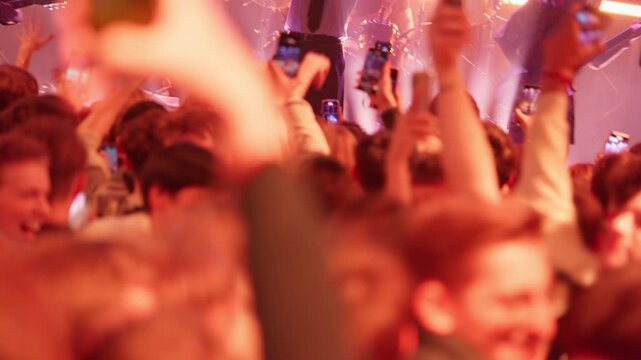 From the crowd's view, fans film a live concert on smartphones. The scene moves through bright stage lights, intense red flashes, and ends in darkness with only glowing screens visible.