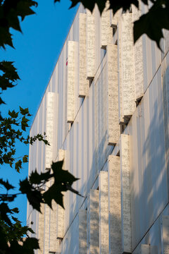 Minimal modern architecture building facade with geometric stone texture against blue sky framed by leaves for abstract urban design