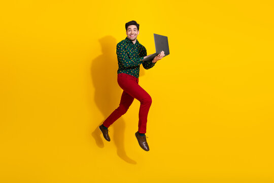 Young man jumps with laptop against bright yellow background expressing energy creativity and fun in a fashion style shoot