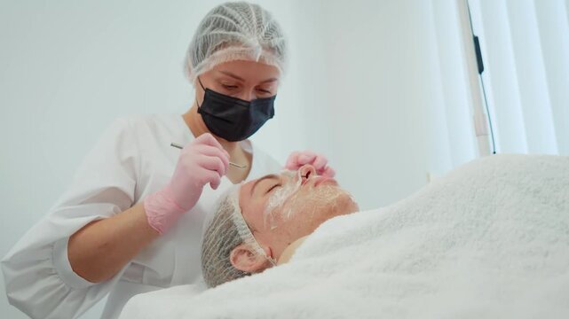 Cosmetologist in mask removing blackheads from forehead of patient. Dermatologist in mask extracting pimples from client forehead. Skin specialist in mask clearing blackheads from woman forehead