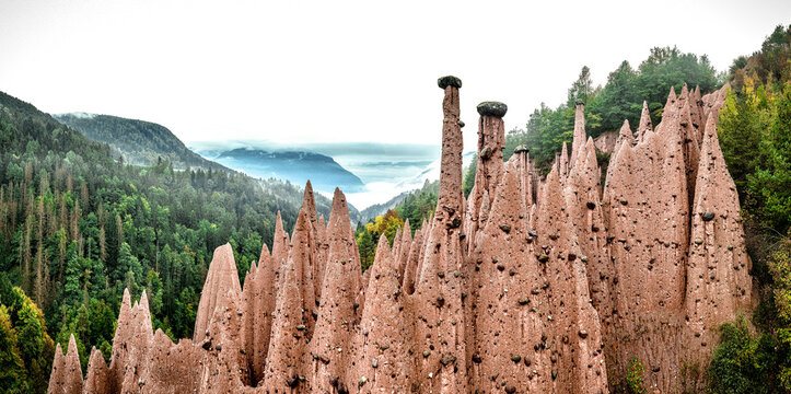 Aerial view of the earth pyramids rise dramatically against the backdrop of verdant forests and distant misty mountains, San Giovanni di Fassa, Trentino-South Tyrol, Italy.