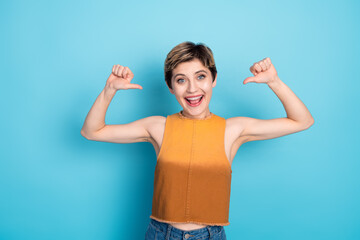 Confident young woman in casual chic orange top poses with arms raised smiling against blue...