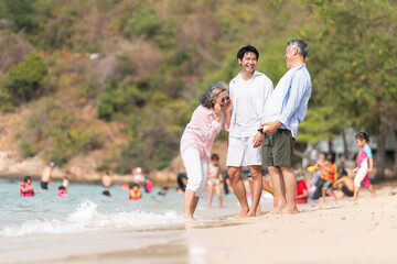 Fototapeta premium In holiday, Senior couple walking with son along the shoreline while talking together