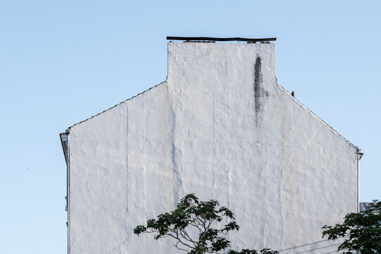 Minimal urban architecture building wall in white texture under sky with tree silhouette creating calm geometry and clean negative space