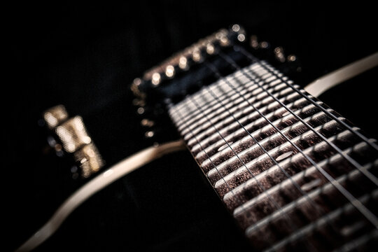 Artistic macro close up of electric guitar fretboard with strings and frets showing detailed wood grain textures against dark background perfect for music instrument and rock wall art themes