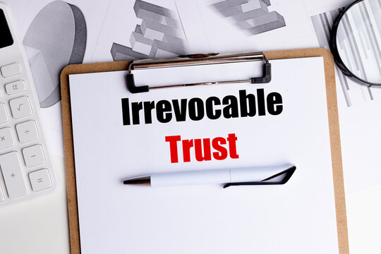 Text irrevocable trust on clipboard with financial documents, calculator and pen on desk 