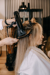 Fototapeta premium Hair care. Blow drying with a special round comb for women's blonde-coloured hair in a beauty salon. Vertical image.