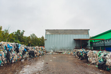 Obraz premium Recycling yard overview. Largescale waste collection site under cloudy sky. Outdoor recycling facility with stacked plastics and processing structures beneath overcast weather