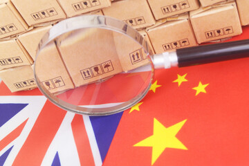 Chinese and British flags with many cardboard boxes and magnifying glass close-up. Trade agreement of China and United Kingdom.