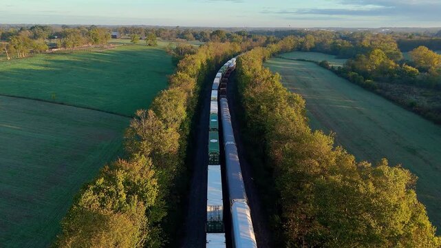 Long cargo train transporting goods through lush fields and trees, symbolizing logistics and commerce