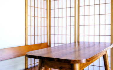 Wooden table in front of Japanese shoji screen with soft natural light. Minimal zen interior background with copy space, ideal for product display, interior design, and presentation concepts