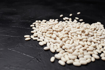 White beans scattered on a dark textured surface, showcasing their smooth, glossy appearance and natural color, ideal for culinary and health-related concepts with copy space