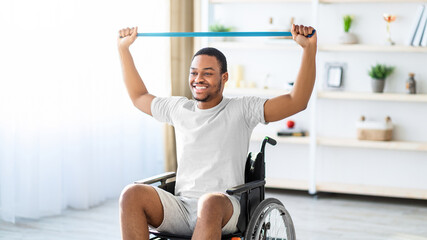 A man with dark skin is smiling while exercising in a wheelchair using a resistance band in a...