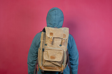 Man wearing a gray hoodie with backpack, standing with his back on red background
