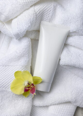 Mockup of white blank squeeze cosmetic tube with yellow orchid flower on bath towel