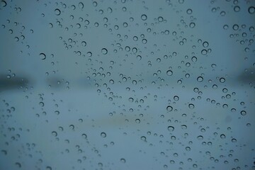 Abstraktes Motiv mit Wassertropfenmuster auf feuchter beschlagener Glasscheibe vor Schneelandschaft mit Feld und Himmel bei Eis, Frost, Sturm und Schnee am Abend im Winter 