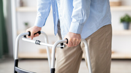 A man with light skin is using a walker in a well-lit room. The setting includes shelves with...