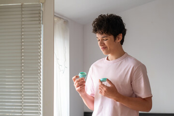 Young man holding skin cream and looking at it in surprise, teenager's daily acne care routine, problematic young skin concept