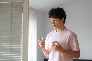 Young man holding skin cream and looking at it in surprise, teenager's daily acne care routine, problematic young skin concept