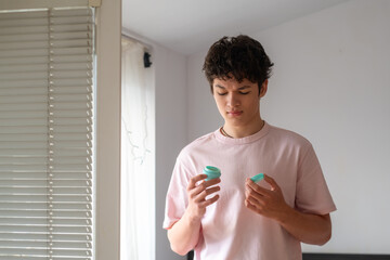 Young man holding skin cream and frowning, teenager's daily acne care routine, problematic young skin concept