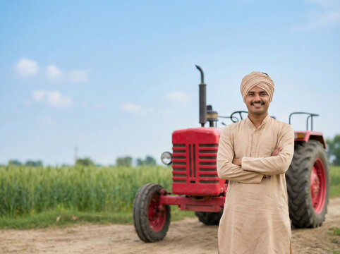 young indian farmer standing with tractor in farmland with copy space representing agriculture finance loans government schemes and rural development concept
