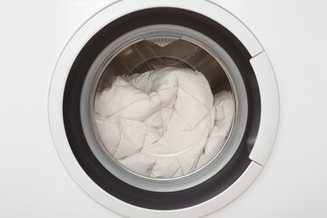 White warm female winter jacket in closed washing machine. Delicate clothes care. Closeup. Front view.