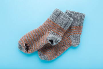 Ripped gray brown knitted socks on light blue table background. Pastel color. Closeup. Top down view.