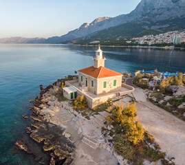 Fototapeta premium Sunrise in Croatia on the Makarska Riviera. Beautiful view of the mountains, city, and lighthouse in Dalmatia.