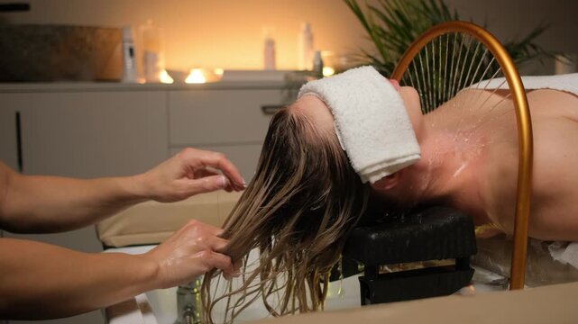 Woman enjoying relaxing hair washing and scalp care treatment in a spa salon with warm ambient lighting.