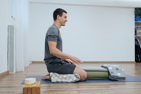 Yoga teacher man in sportswear explains how to use props practicing yoga for more comfortable relaxation indoor