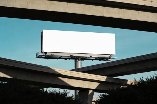 Blank highway billboard mockup with clear blue sky standing high above concrete freeway overpasses with copy space for advertising and communications concept.