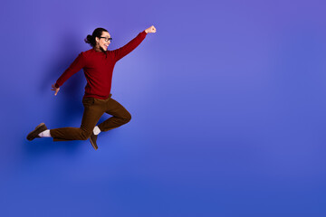 Fototapeta premium Young handsome man jumping with joy in a purple studio background wearing a red sweater and brown pants